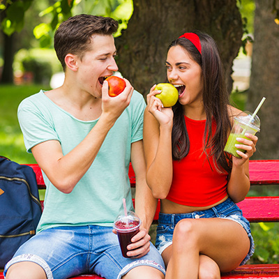 Junges Paar auf der Parkbank mit Äfeln und Smoothies